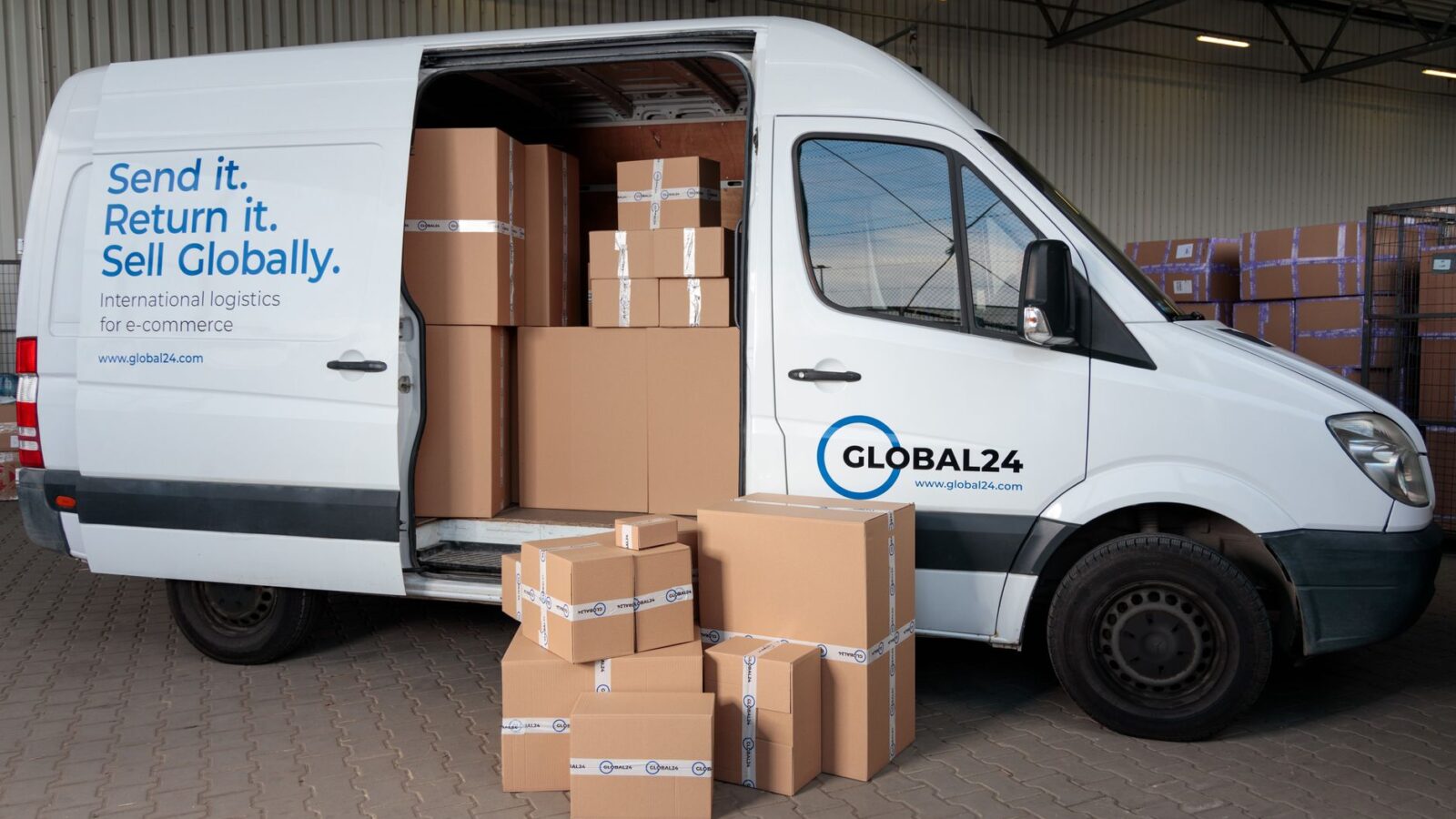 Stack of returned cardboard shipping boxes on a warehouse floor beside a parked delivery van