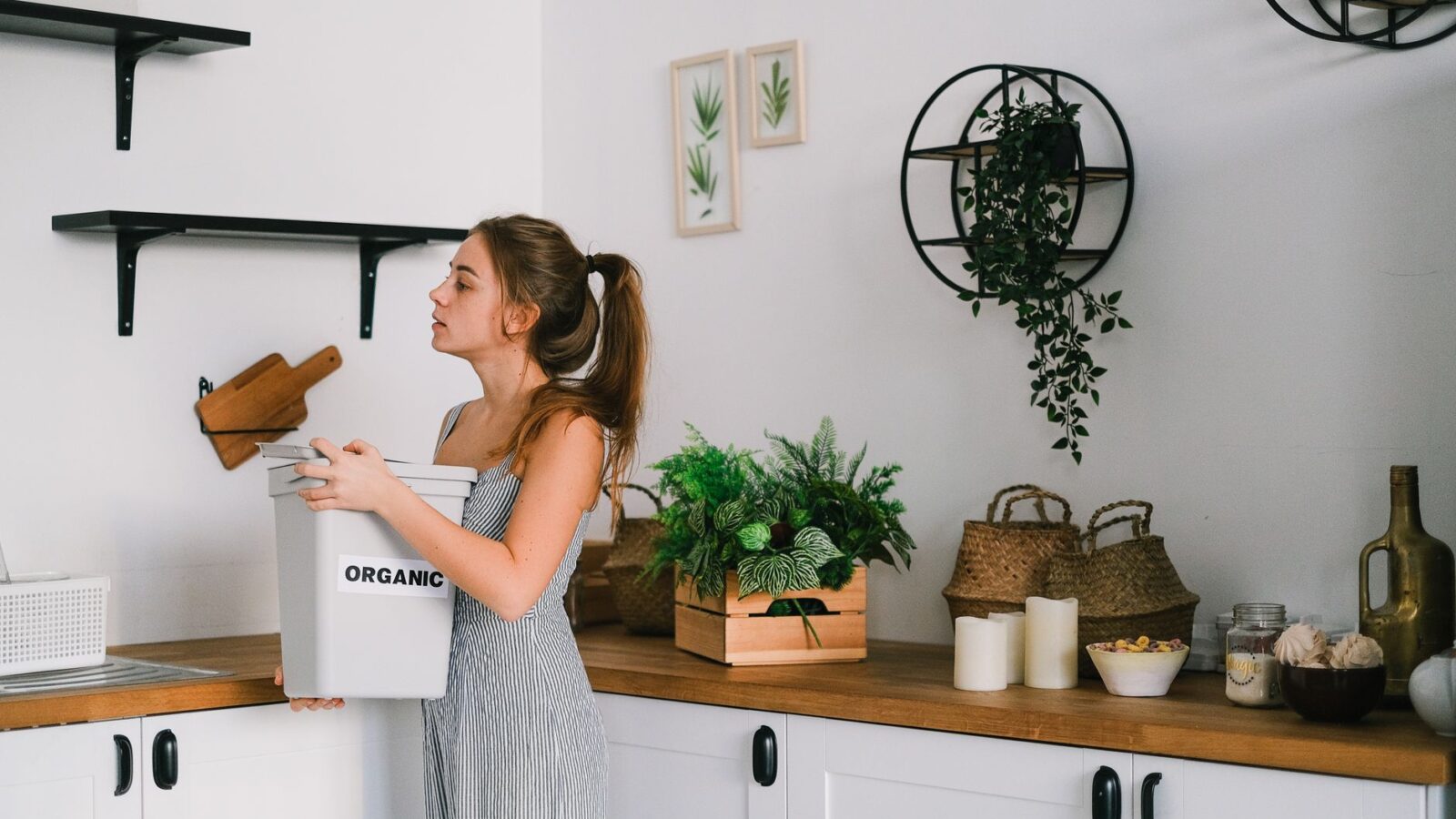 Roommates sorting food scraps and recycling at a labeled bin station in a shared kitchen.